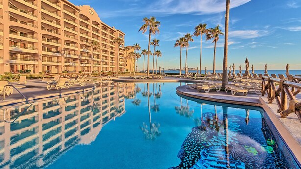 A hotel with multiple floors, a pool with clear blue water, and palm trees. - Penthouse Beachfront at Sonoran Spa (Puerto Peñasco)