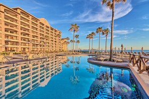 A hotel with multiple floors, a pool with clear blue water, and palm trees. - Penthouse Beachfront at Sonoran Spa (Puerto Peñasco)