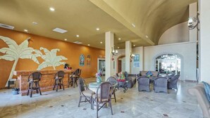 A spacious lobby with a reception desk, wicker furniture, and a large mural of leaves. - Penthouse Beachfront at Sonoran Spa (Puerto Peñasco)
