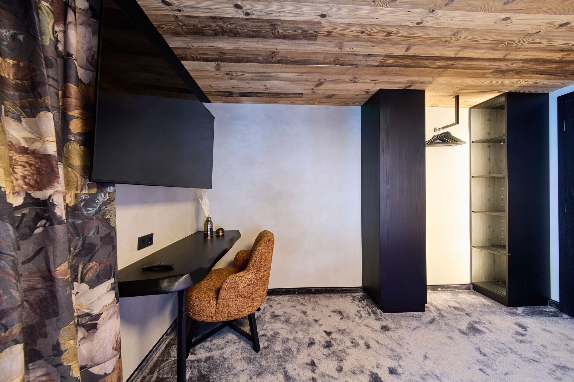 A modern room with a wooden ceiling, a black desk, a brown chair, and a large wardrobe.