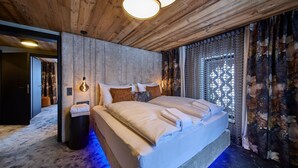 Un dormitorio moderno con techo de madera, una cama grande con ropa blanca, una mesita de noche y una ventana con cortinas estampadas.