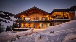 Una casa moderna de dos pisos con fachada de madera, ventanas amplias y un balcón con vista a un paisaje nevado.