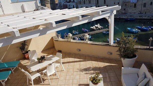 Una terraza con mobiliario de mimbre blanco, una planta en maceta y vista a un canal con barcos.