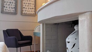 Habitación con chimenea, ilustraciones náuticas enmarcadas, una silla negra y una pequeña escultura de coral azul y blanco.