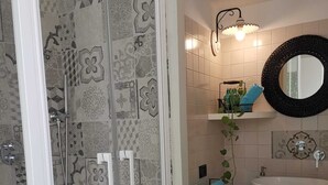Un baño con baldosas estampadas, ducha envuelta en vidrio, lavamanos blanco, espejo y toallero.