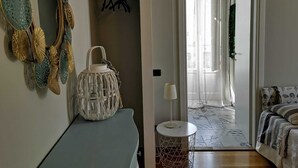 Una habitación con cama, una mesita pequeña, una lámpara colgante, un perchero y una puerta que da a un balcón.