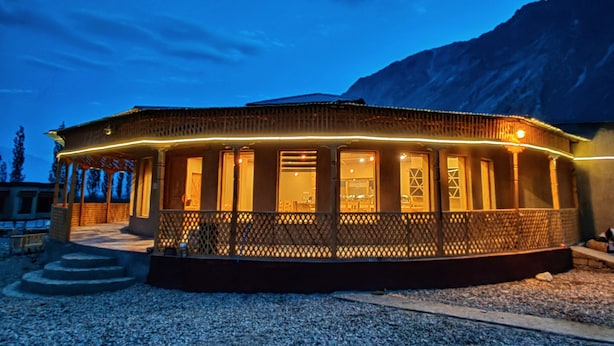 A building with a covered patio area, a gravel driveway, and a mountainous backdrop. - White Sands Resort- Best Resort in NUBRA (Leh)