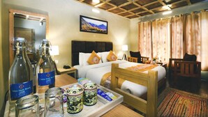A hotel room with a wooden ceiling, a bed with white bedding, a desk with a tray of items, and a large window with curtains. - White Sands Resort- Best Resort in NUBRA (Leh)