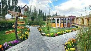 A garden pathway leading to a gazebo with a signpost indicating a restaurant, games room, and health center. - White Sands Resort- Best Resort in NUBRA (Leh)