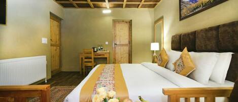 A hotel room with a large bed, wooden headboard, a desk with a chair, a radiator, and a framed picture on the wall.