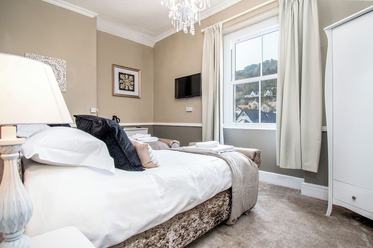 A neatly arranged bedroom with a bed, a television, and a window with curtains.