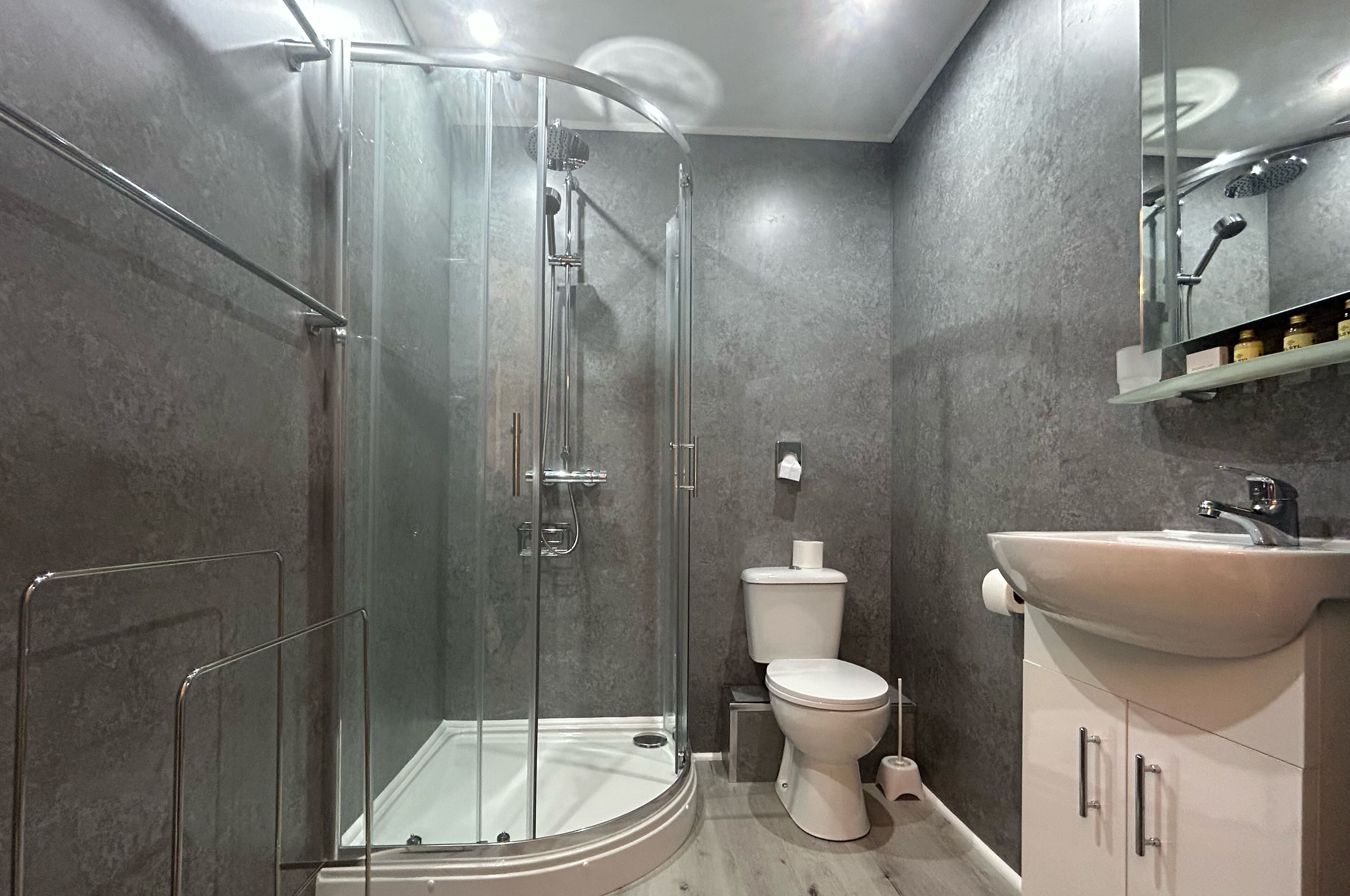 A modern bathroom with a glass-enclosed shower, a white toilet, and a sink with a mirror above it.