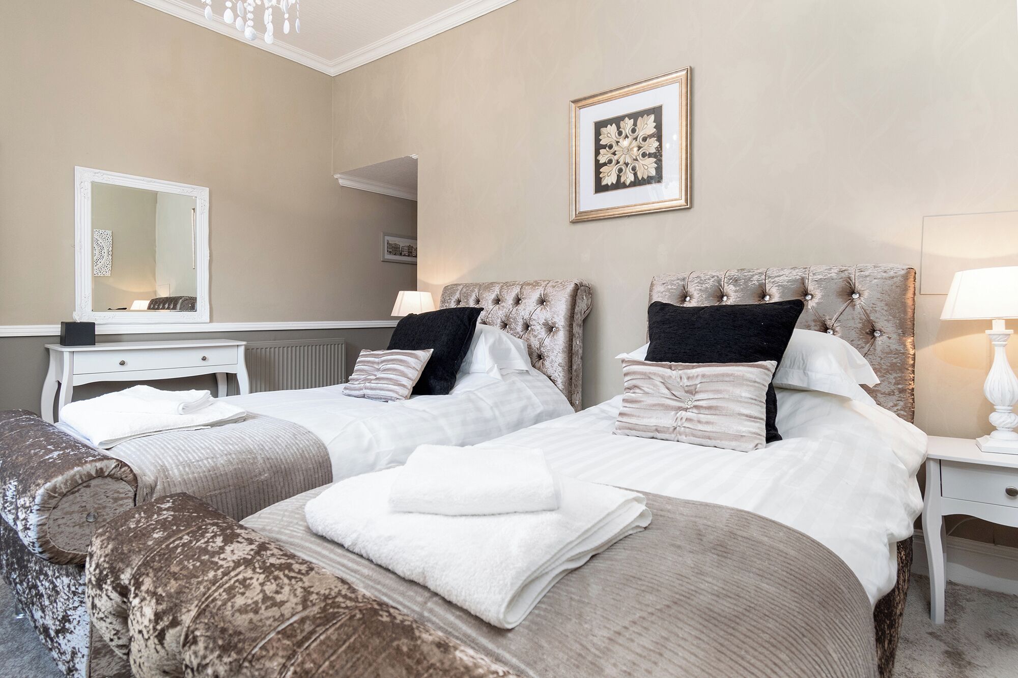 A hotel room with two beds, a dresser, a mirror, a framed picture on the wall, and a lamp on the nightstand.