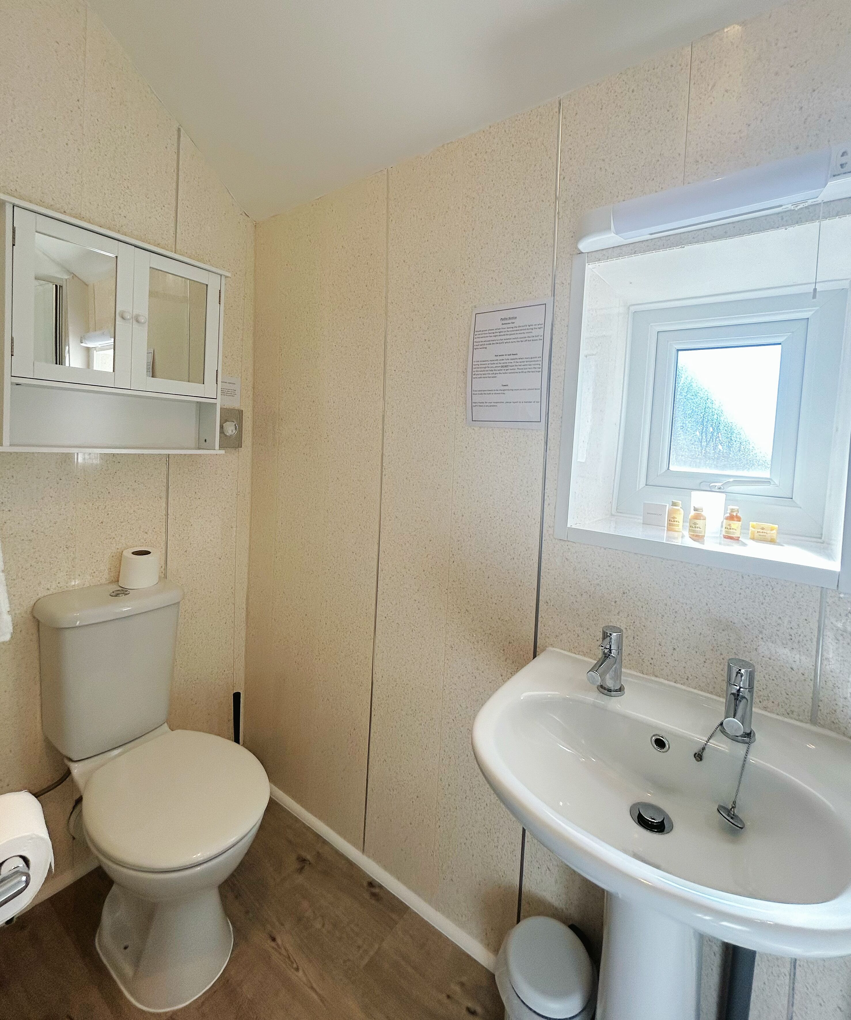 A bathroom with a toilet, sink, mirror, and window.
