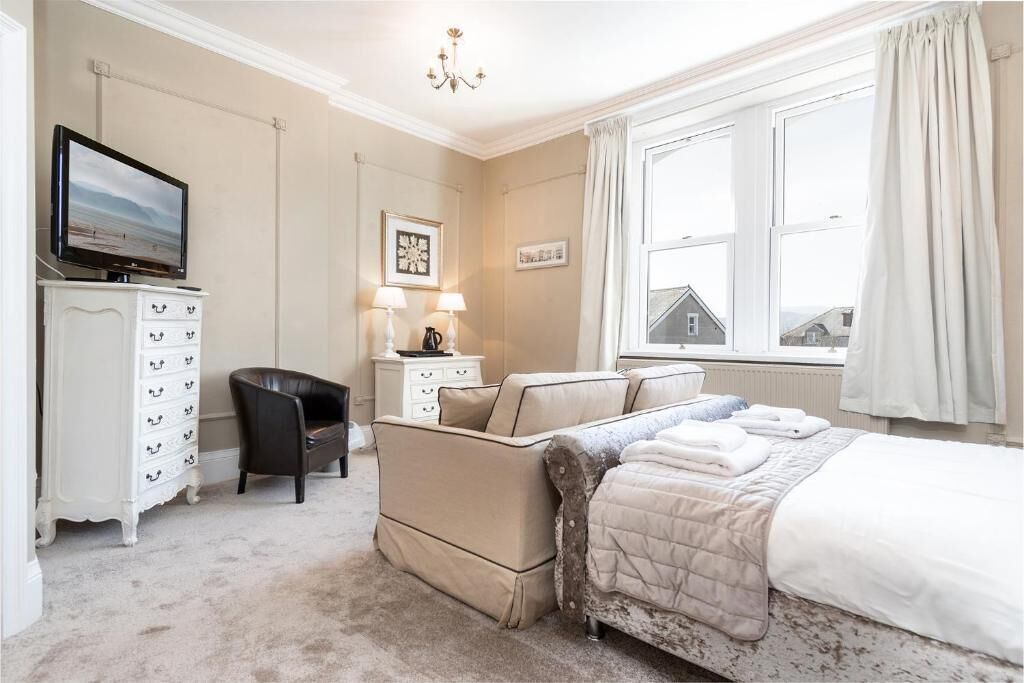 A bedroom with a bed, a TV, a dresser, a chair, and a window with curtains.