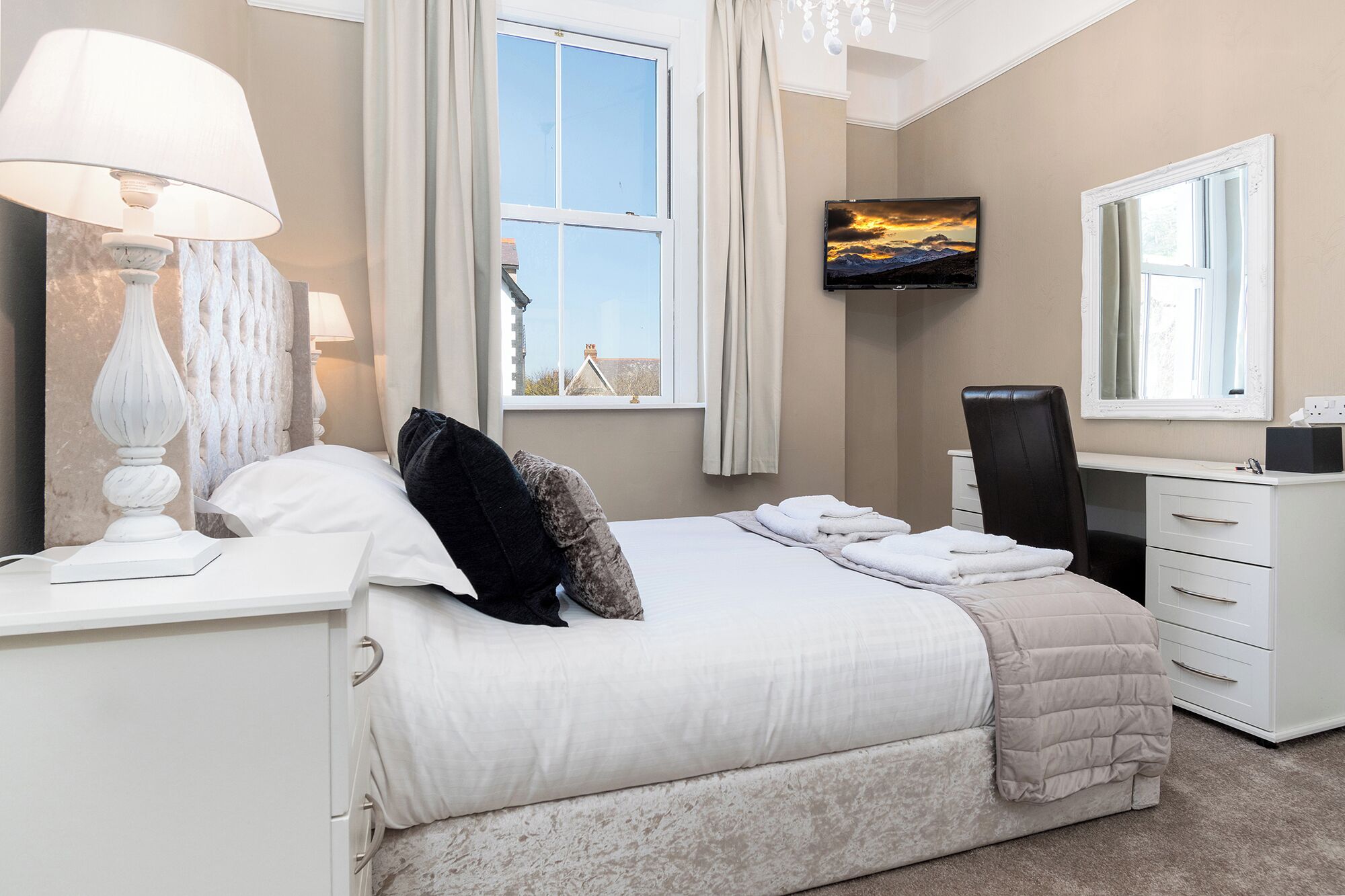 Een hotelkamer met een bed, een bureau, een stoel, een televisie en een raam met gordijnen.