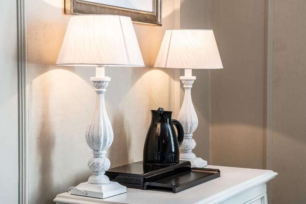 Une console blanche, agrémentée de deux lampes blanches et d’une cafetière noire.