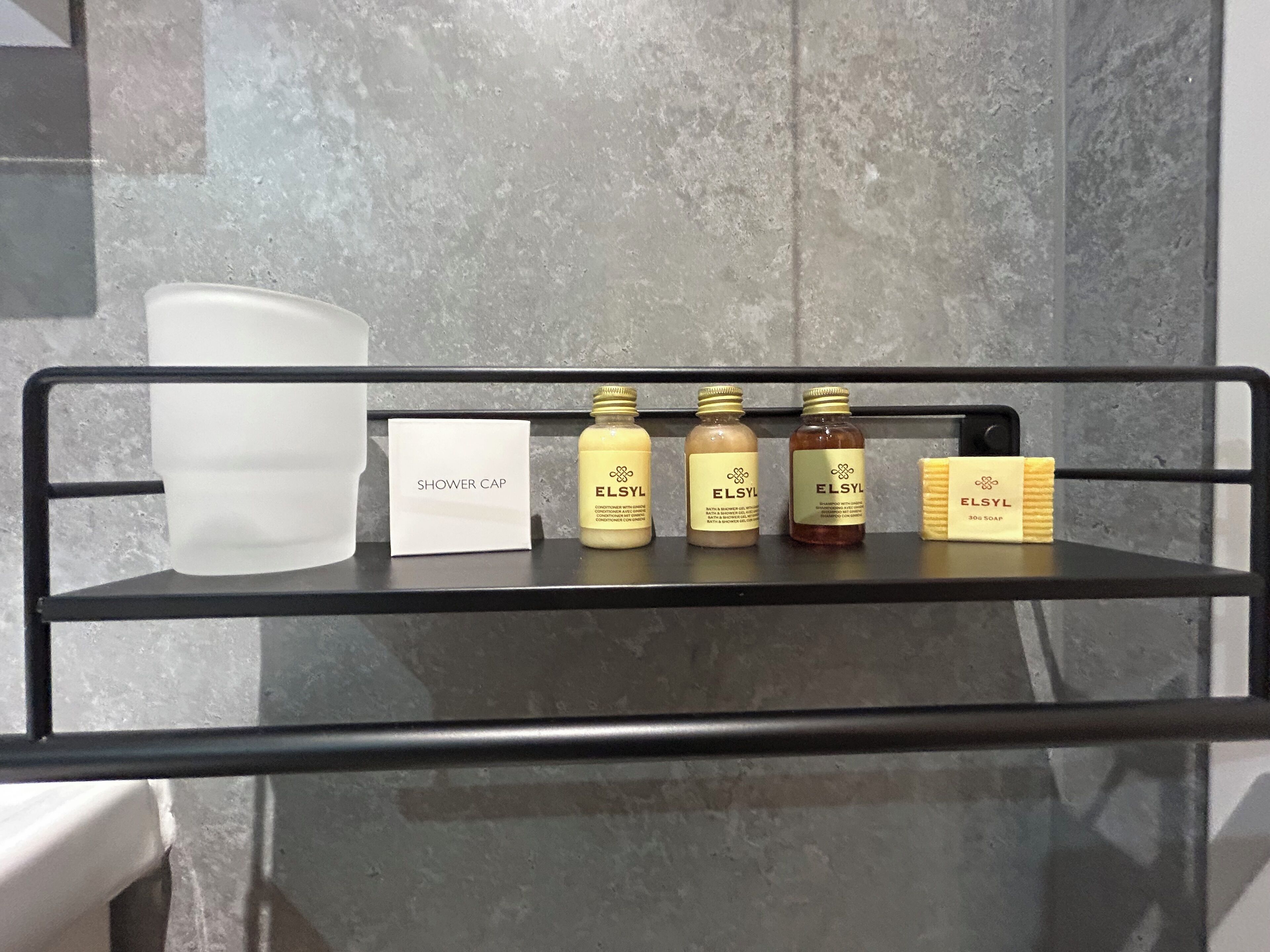 A shower area with a metal shelf holding toiletries, a shower cap, and a soap dispenser.