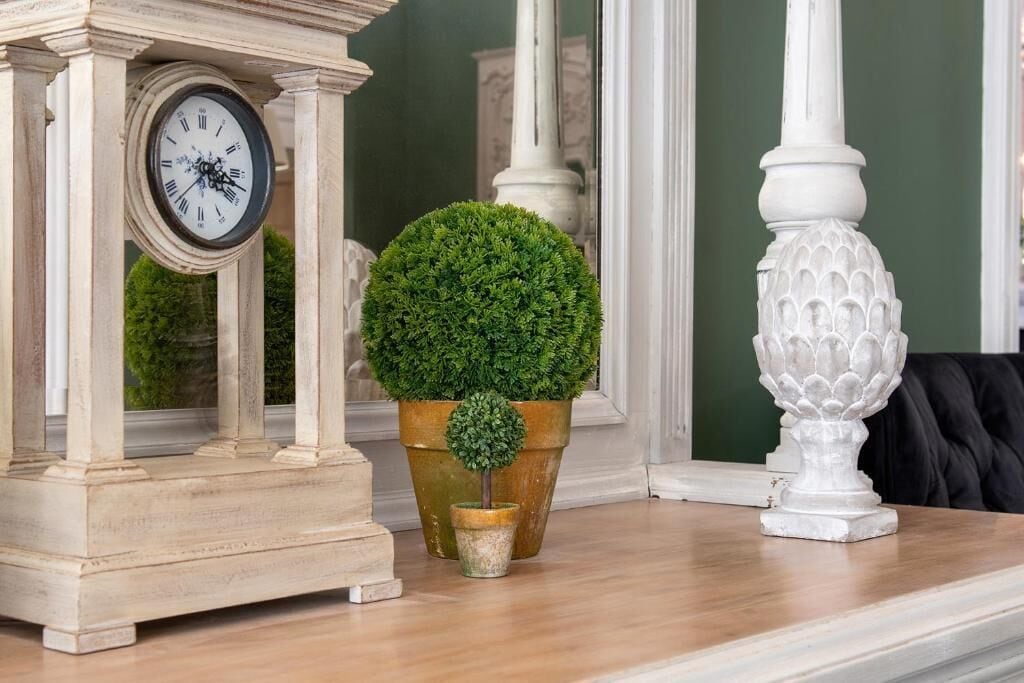 A clock, a potted plant, and a decorative vase on a wooden surface.