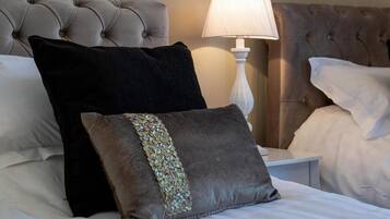 Una cama bien hecha con un cabecero capitonado, una mesita de noche blanca y una lámpara.