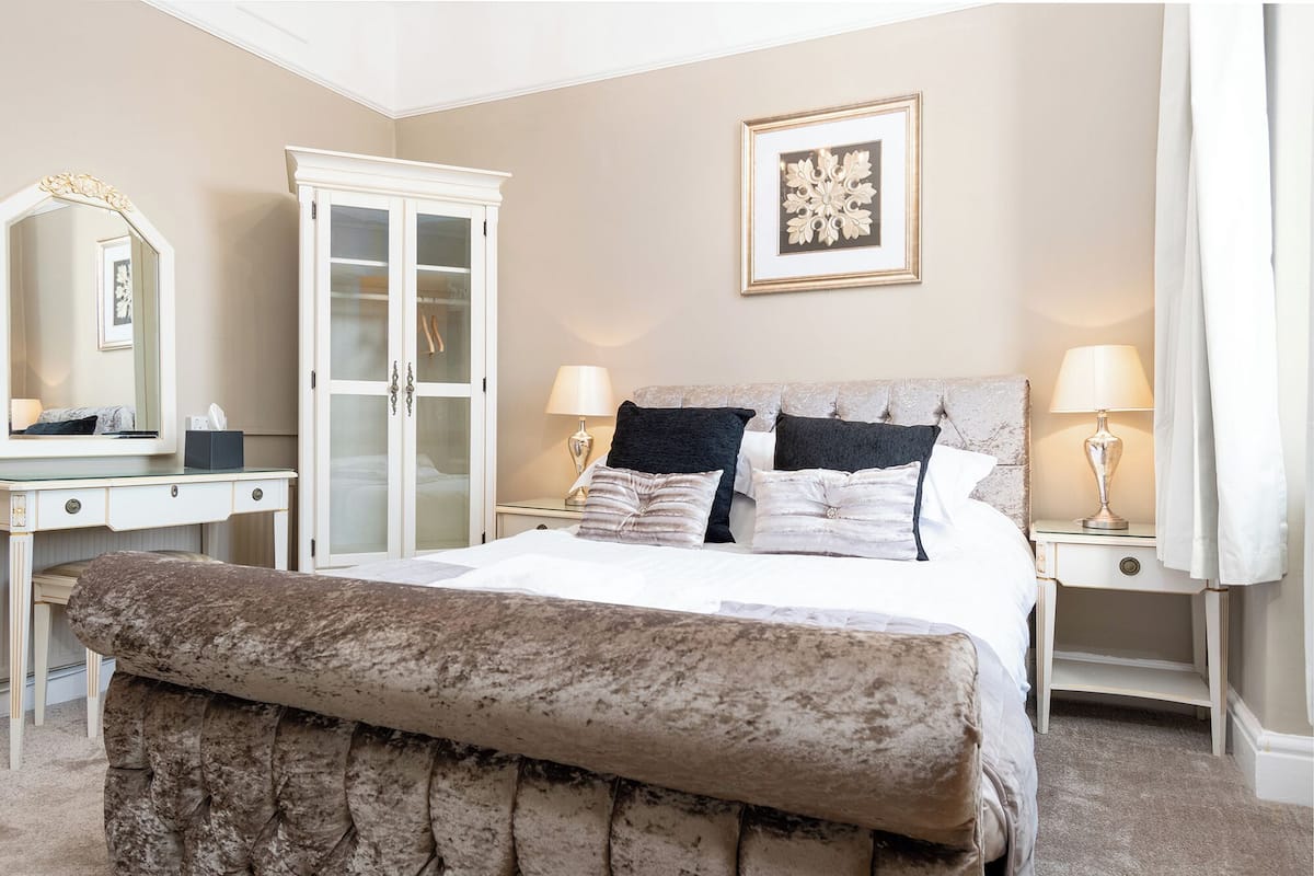 A bedroom with a large bed, a wardrobe, a dressing table, and a mirror.