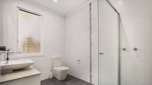 Un baño moderno con cabina de ducha de vidrio, inodoro blanco y lavamanos con espejo.