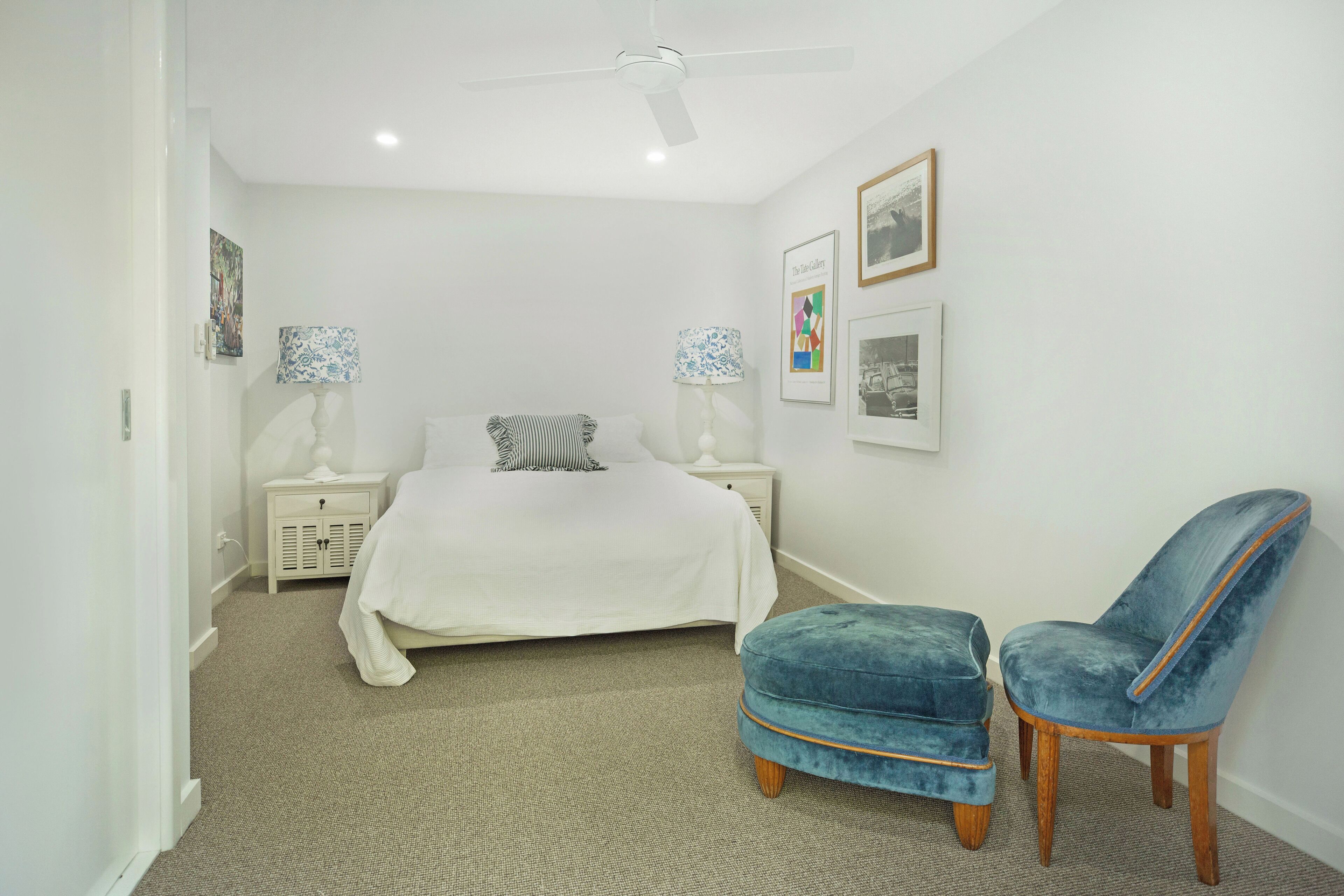 A bedroom with a bed, two nightstands, two lamps, a ceiling fan, and a blue chair.