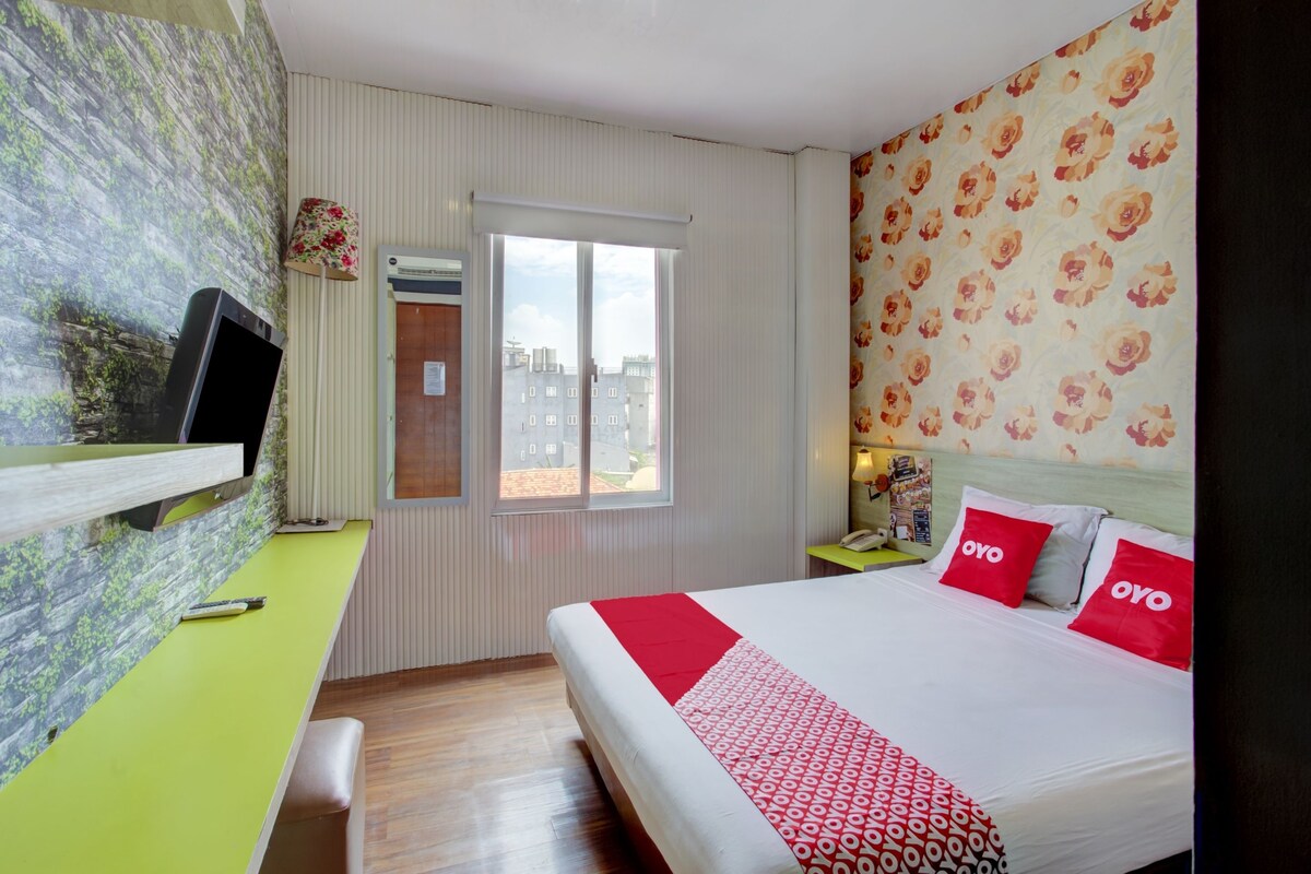 A hotel room with a bed, a desk, a television, a window, and a patterned wall.