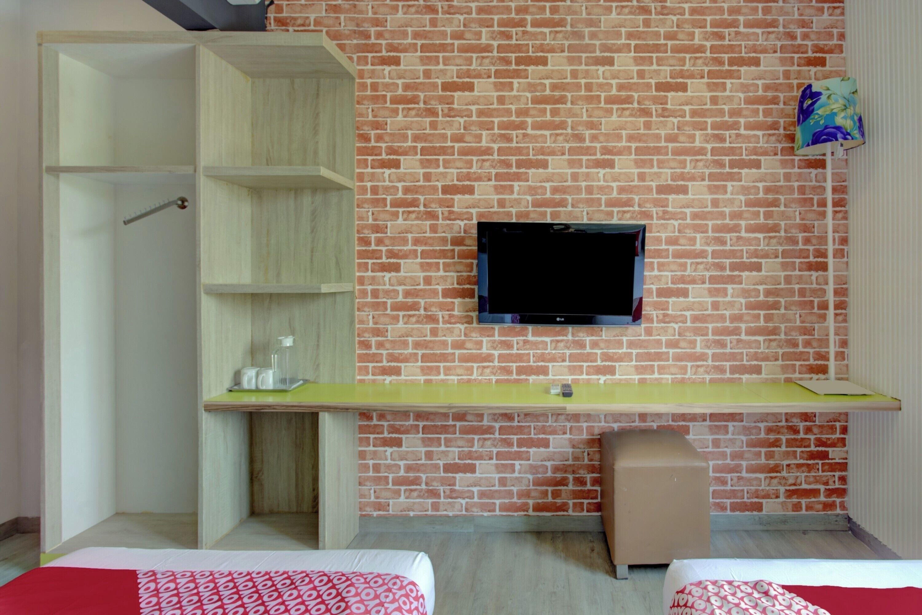 A room with a brick wall, a mounted TV, a desk with a chair, and two beds.