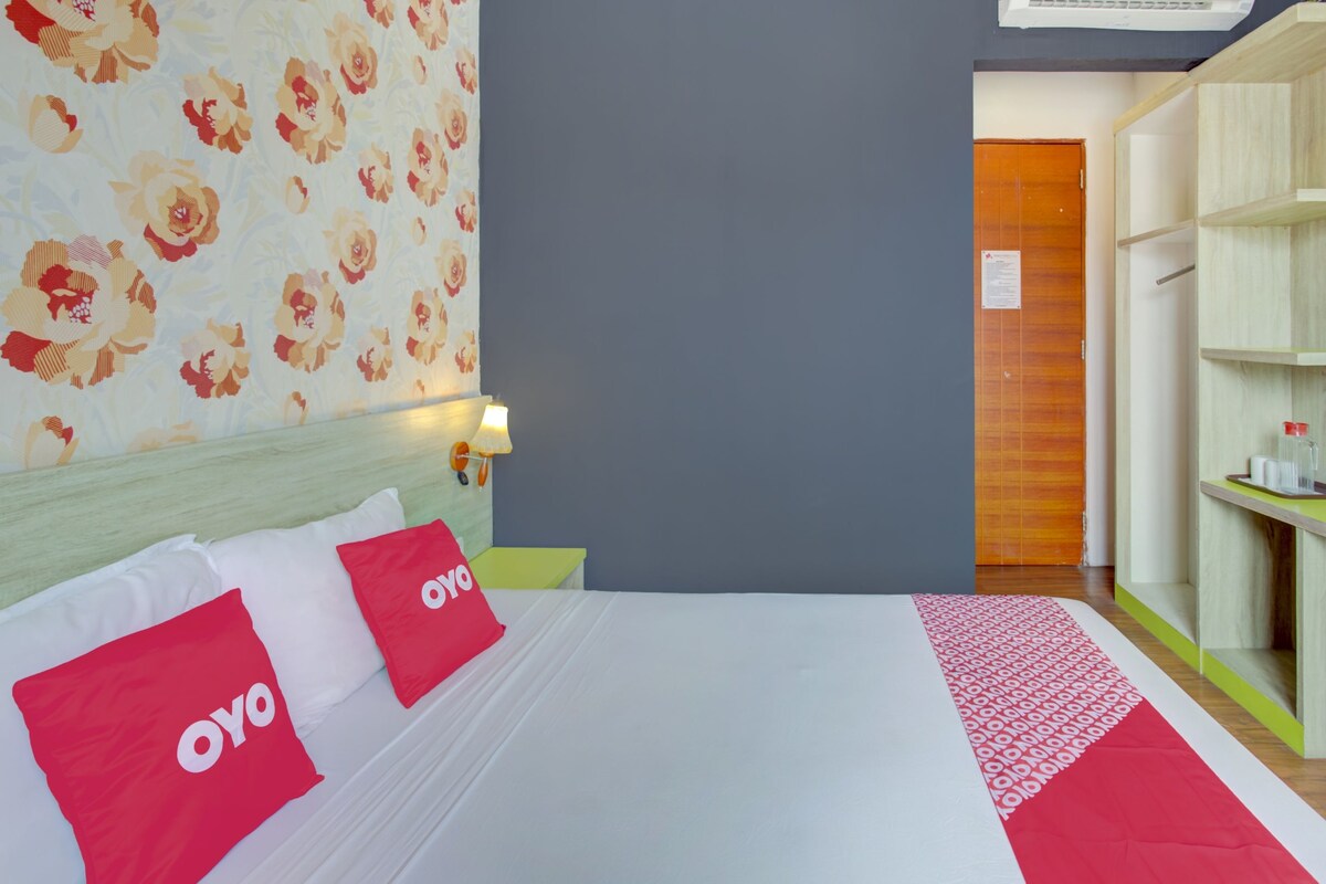 A hotel room with a bed, pillows with 'oyo' branding, a floral wallpaper, and a wooden wardrobe.