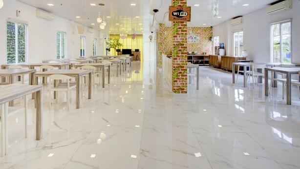 A spacious, well-lit dining area with multiple tables and chairs, a brick pillar with a Wi-Fi sign, and a clean, polished floor. - Collection O Gambir Near Masjid Istiqlal Formerly Aleander Hotel (Jakarta)