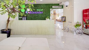 A hotel reception area with a green wall, a reception desk, a potted tree, a bicycle, and a Coca-Cola advertisement. - Collection O Gambir Near Masjid Istiqlal Formerly Aleander Hotel (Jakarta)