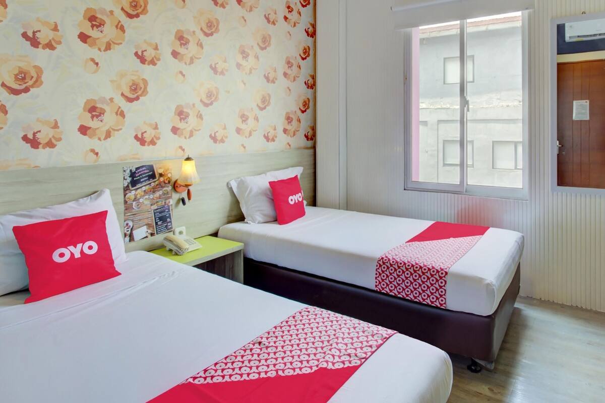 A hotel room with two beds, floral wallpaper, a window, a desk, and a chair.