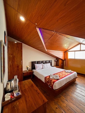 Un dormitorio con techo de madera, una cama con ropa de cama blanca, una mesita de noche con lámpara y un banco de madera con artículos de aseo.