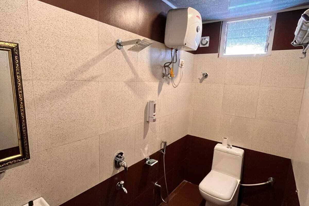 Baño pequeño y funcional con inodoro, bidé y lavamanos. Cuenta con un espejo, dispensador de jabón y un ventanal.