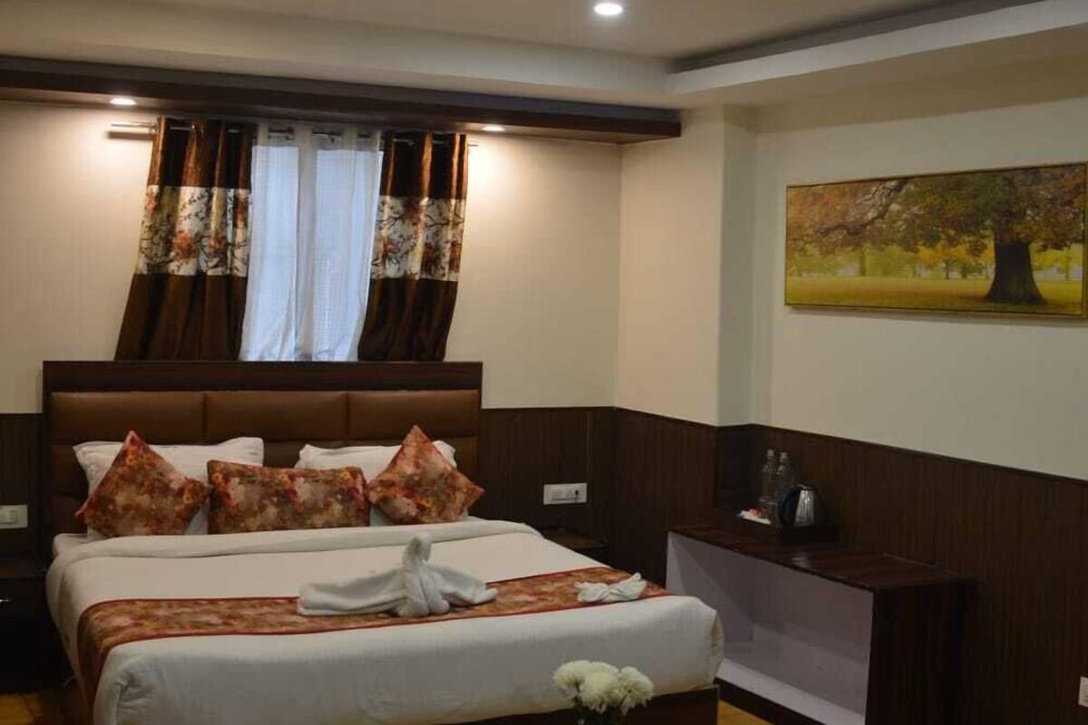 Una habitación de hotel con una cama grande, cabecero de madera, una mesita de noche con un florero y un cuadro en la pared.