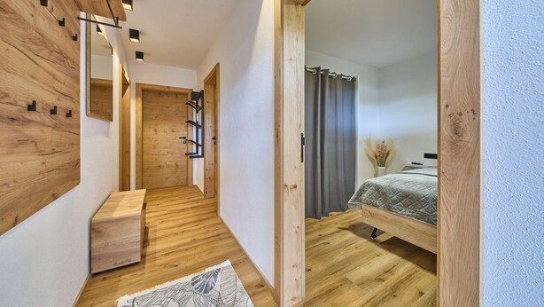 Un pasillo estrecho con paredes y puerta de madera que dan a un dormitorio con cama y ventana con cortinas.