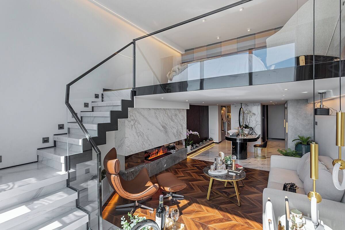 Un interior moderno con una escalera de cristal, una chimenea, asientos de cuero y una zona de comedor.