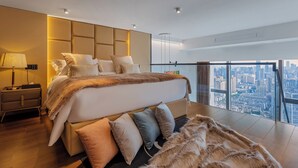 A modern bedroom with a large bed, a nightstand, a fur throw, and a city view through floor-to-ceiling windows. - Hotel high sky view hotel (Kunming)