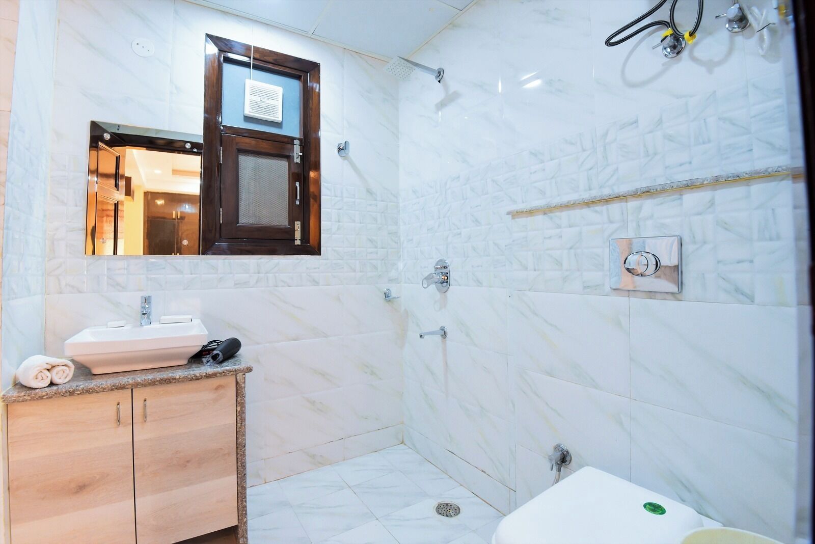 A bathroom with a marble sink, wooden vanity, a shower area, and a small window.