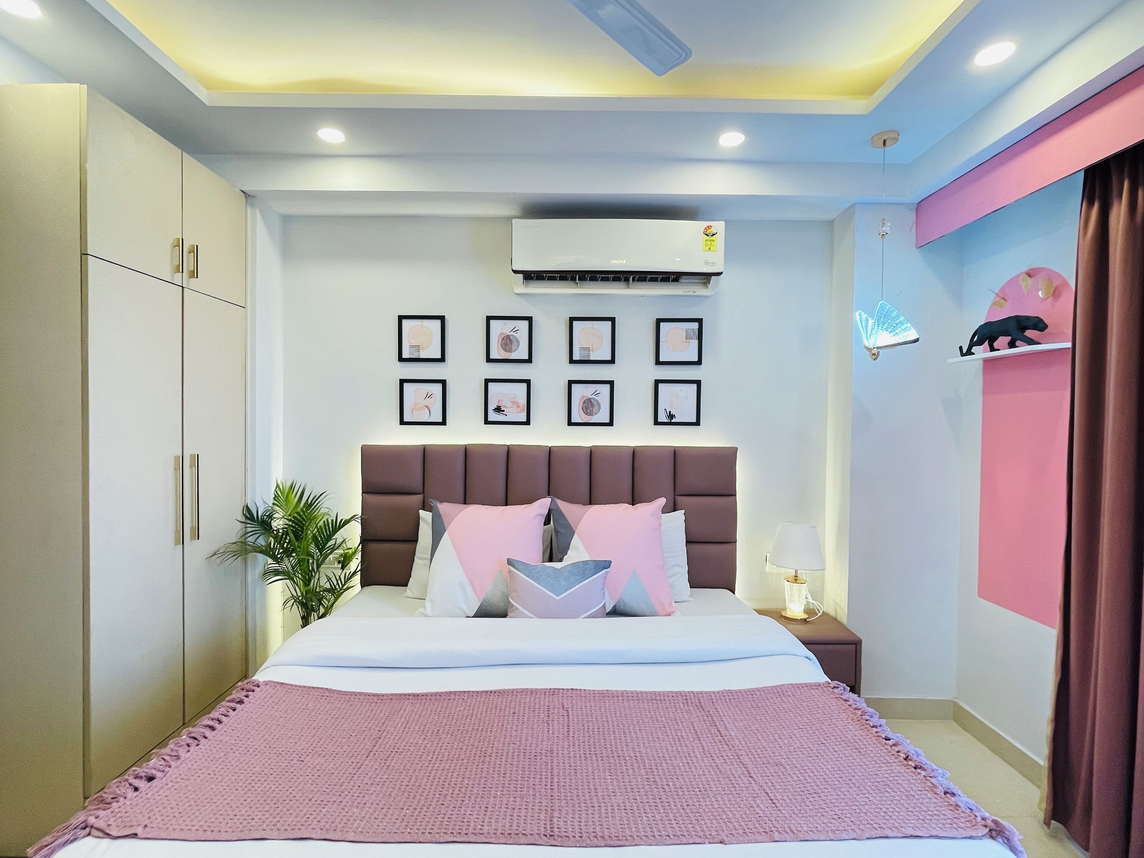 A modern bedroom with a large bed, a wall-mounted air conditioner, and a bedside table with a lamp.