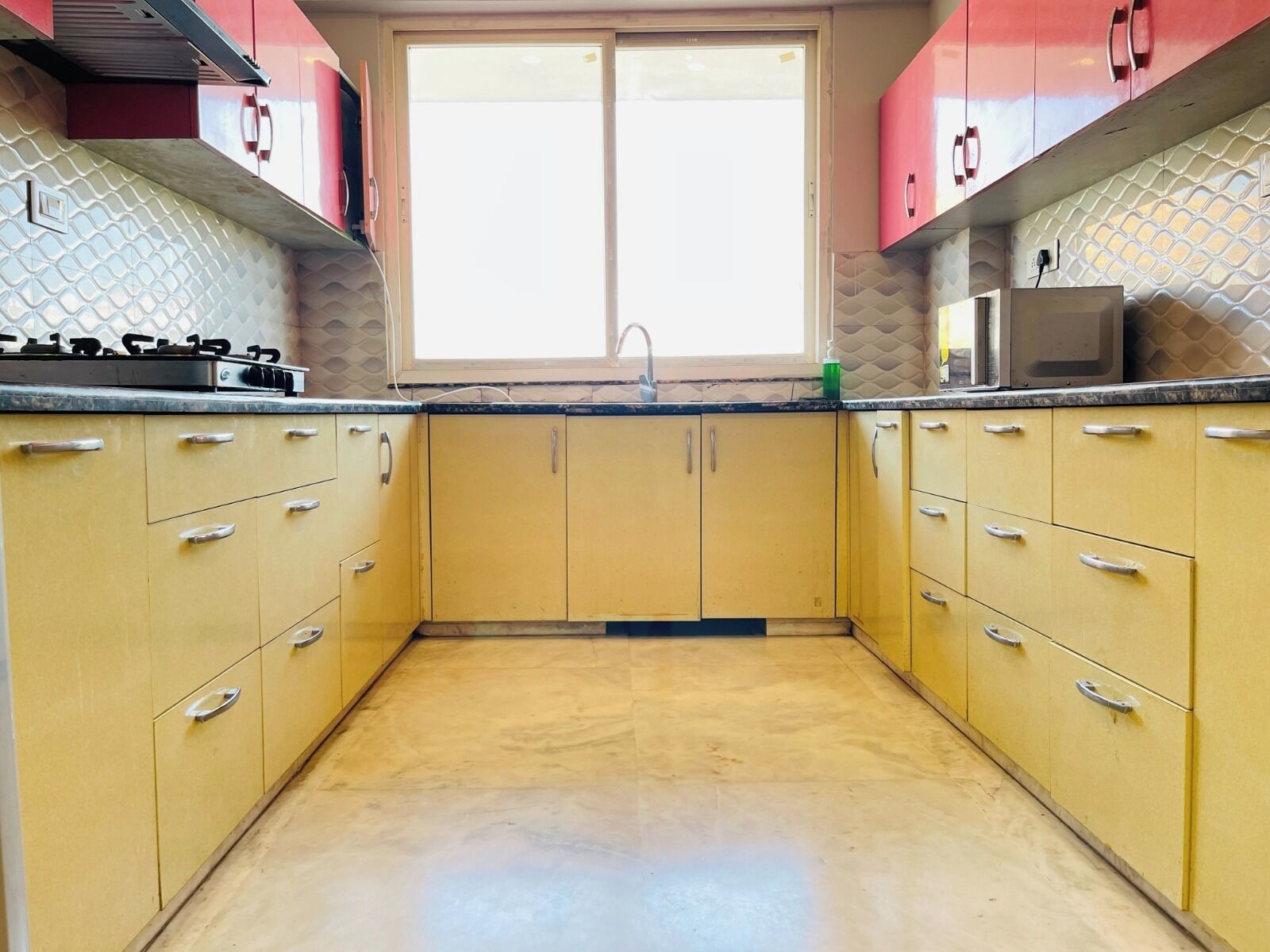 A kitchen with yellow cabinets, a window, and a microwave on the countertop.