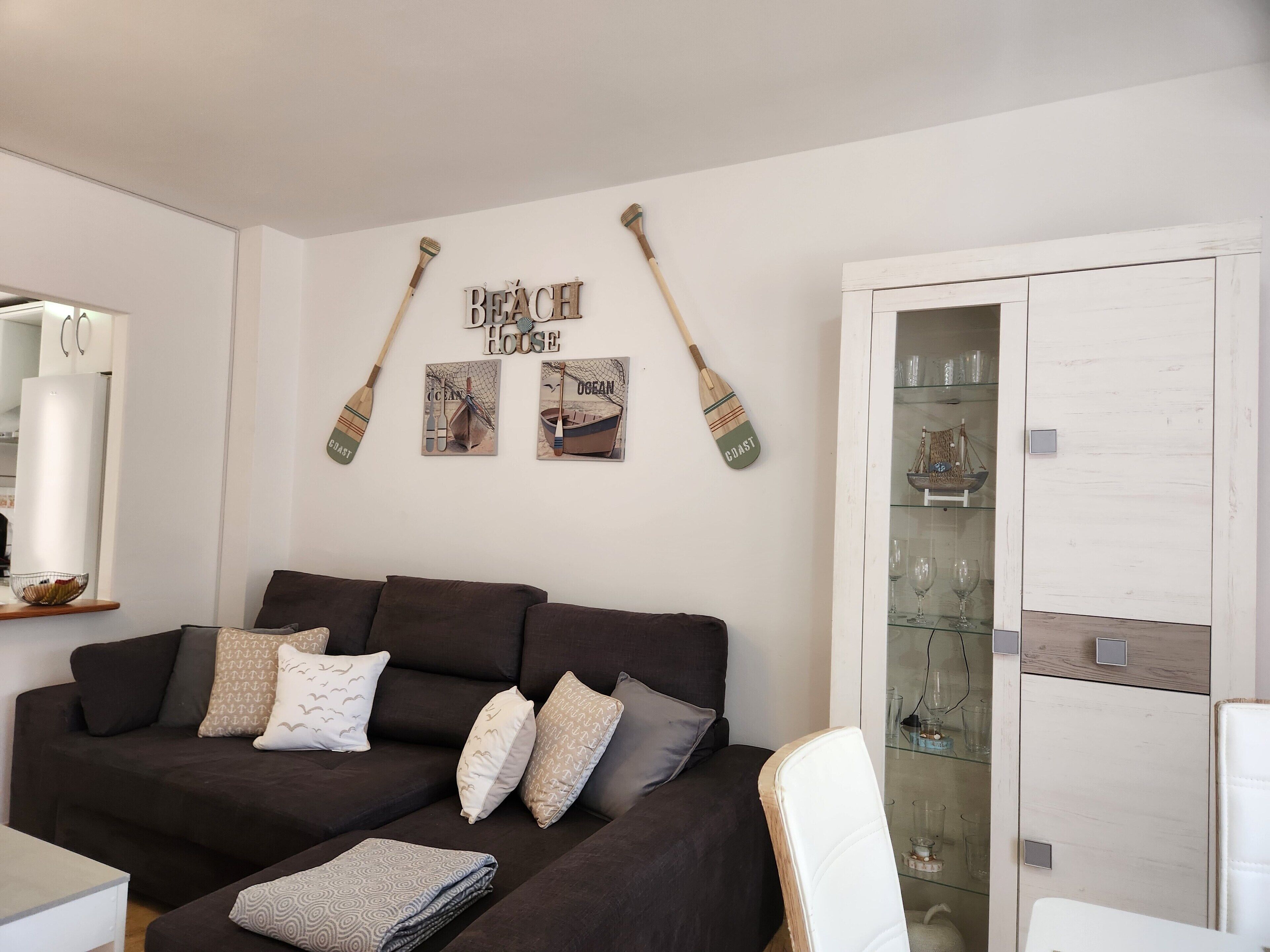 En stue med en mørkebrun sofa, to surfbræder på væggen og et glashus med pynteting.