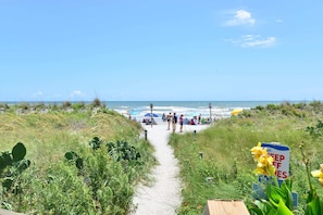 A beach path leading to the ocean with people and beach umbrellas.