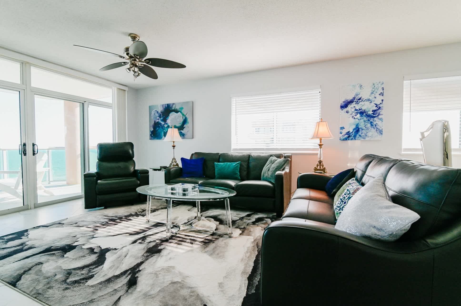 A living room with a glass coffee table, two sofas, a ceiling fan, and artwork on the walls.