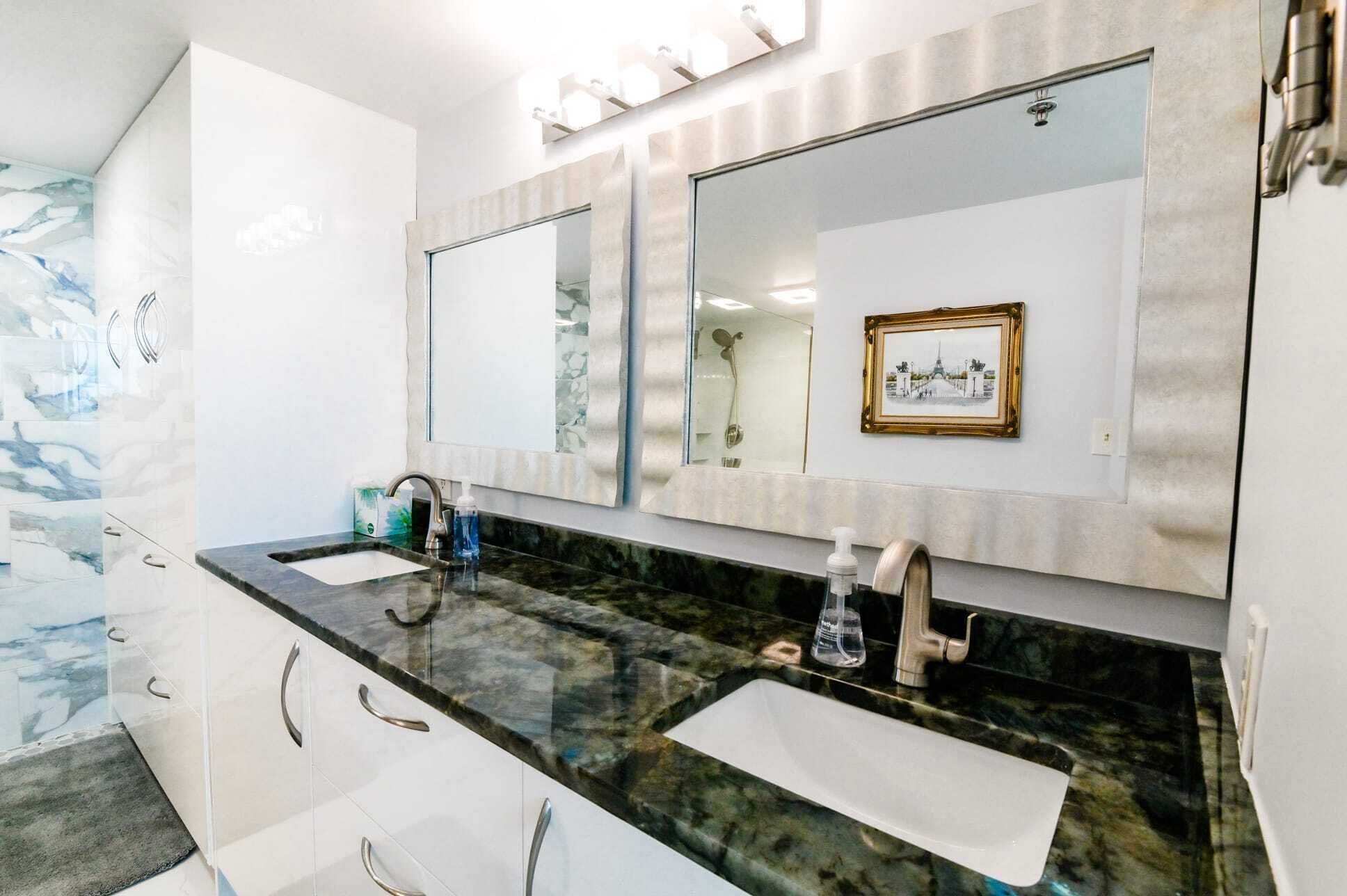 Une salle de bain avec deux lavabos, un grand miroir et un tableau encadré au mur.
