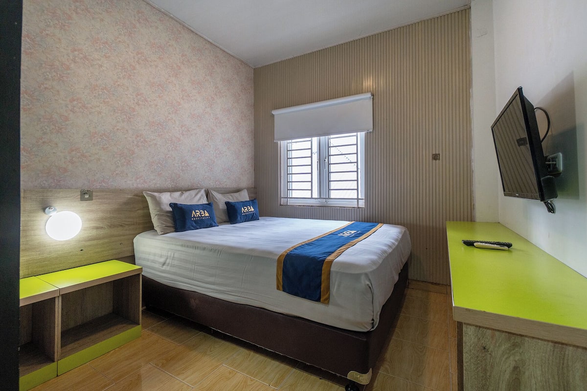 Quarto de hotel com cama, escrivaninha, televisão e janela.