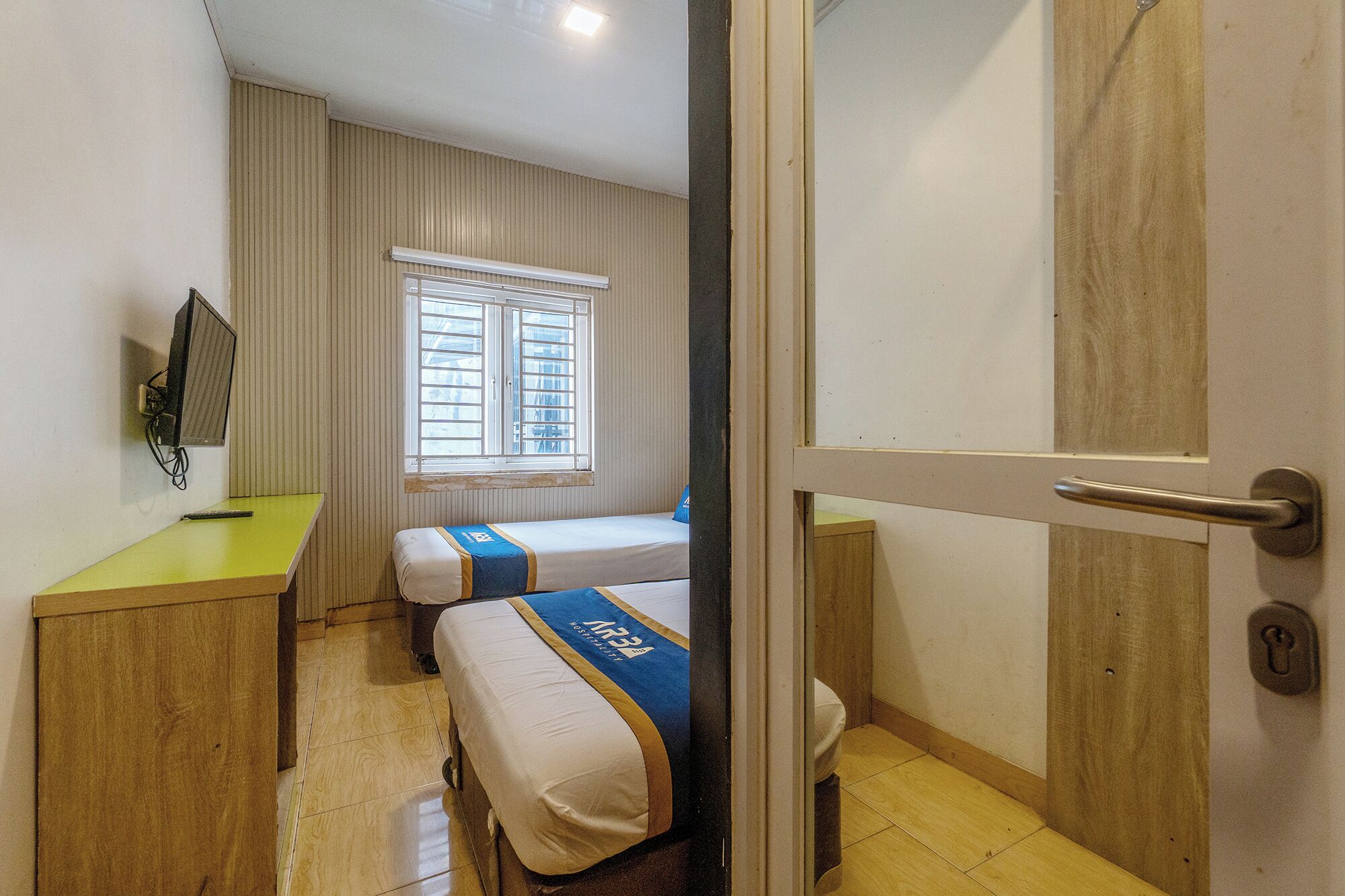 Une chambre d’hôtel avec deux lits, une télévision, une fenêtre avec des stores et une porte.