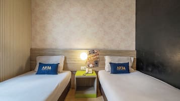 A hotel room with two beds, a nightstand with a phone, a wall clock, and a floral wallpaper.