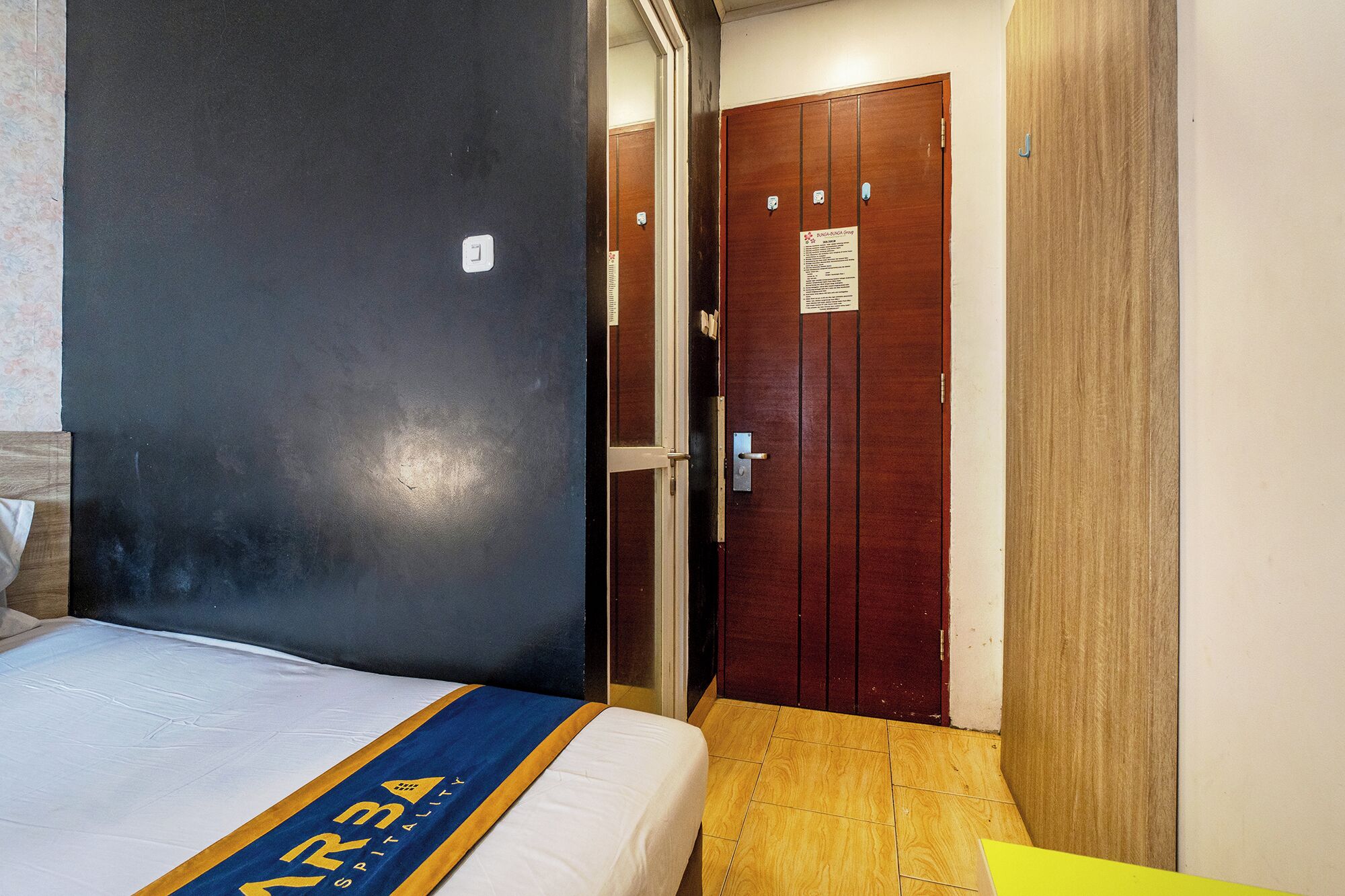 A hotel room with a bed, a wooden wardrobe, and a door with a sign.